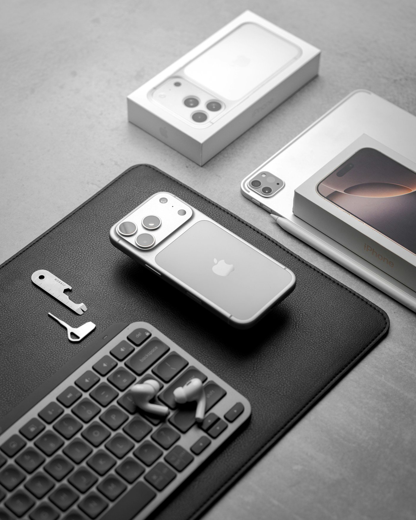 Silver smartphones, an open earbud case and desk accessories arranged on a dark desk mat; reference photography