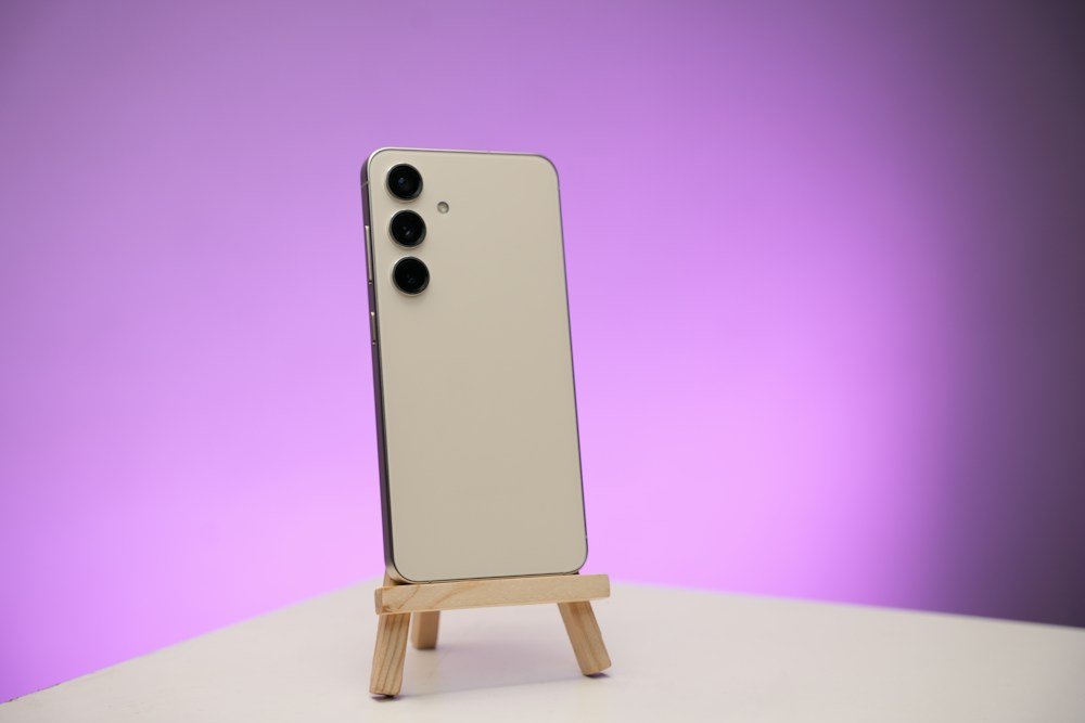 Stock photograph of a cream Galaxy S24 on a wooden stand, not an actual pre-owned unit